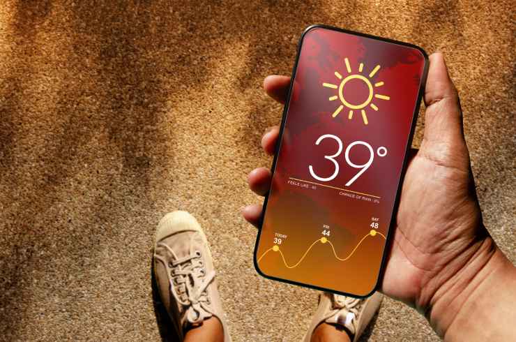 Smartphone in mano sotto il sole che segna 39°