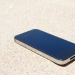 Smartphone in spiaggia, appoggiato sopra la sabbia e lasciato sotto il sole