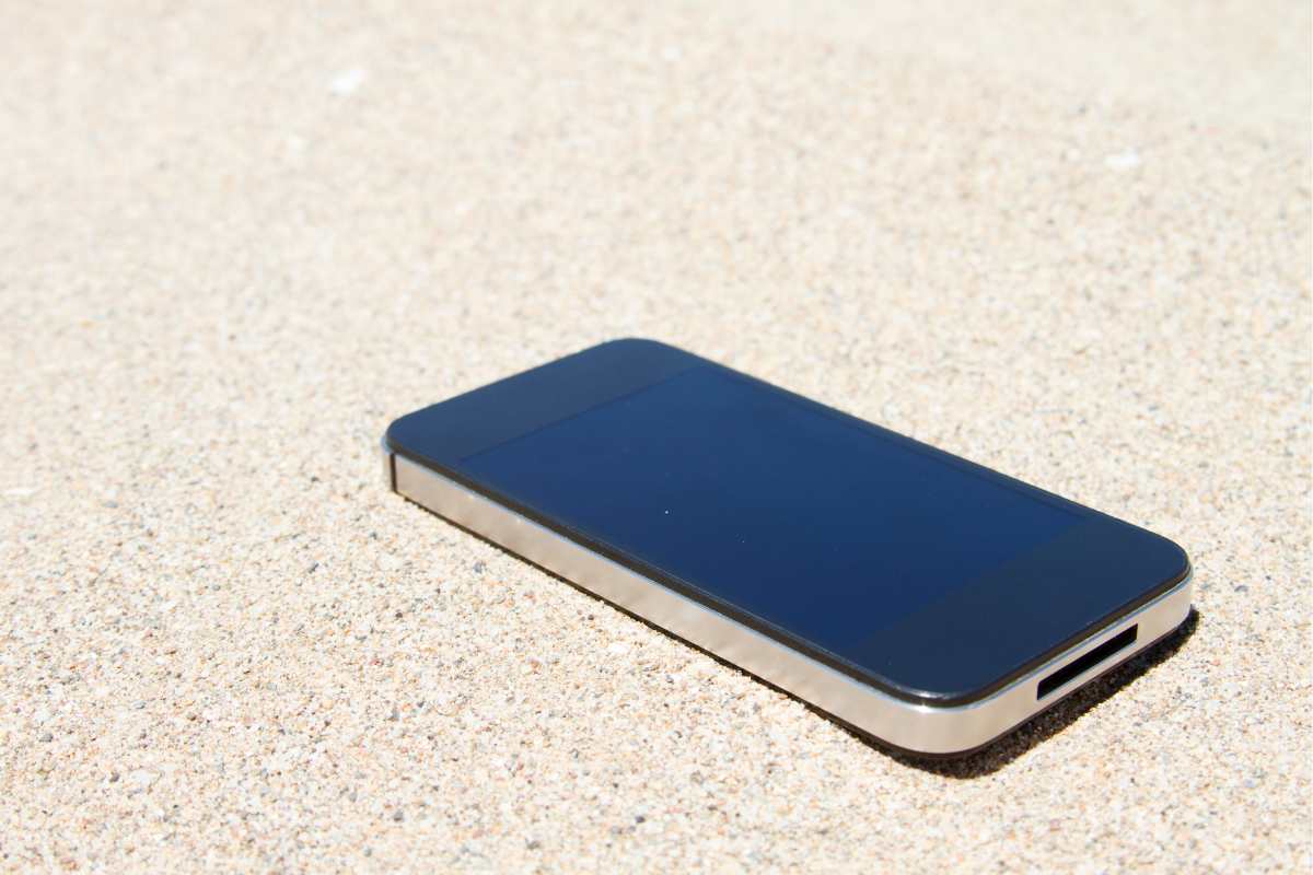 Smartphone in spiaggia, appoggiato sopra la sabbia e lasciato sotto il sole